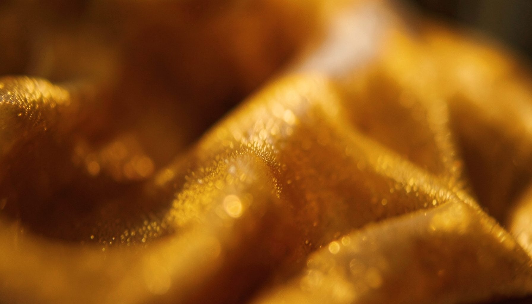 Soft-focus close-up of warm amber and gold fabric textures with a gentle bokeh background, evoking an intimate dramatic mood